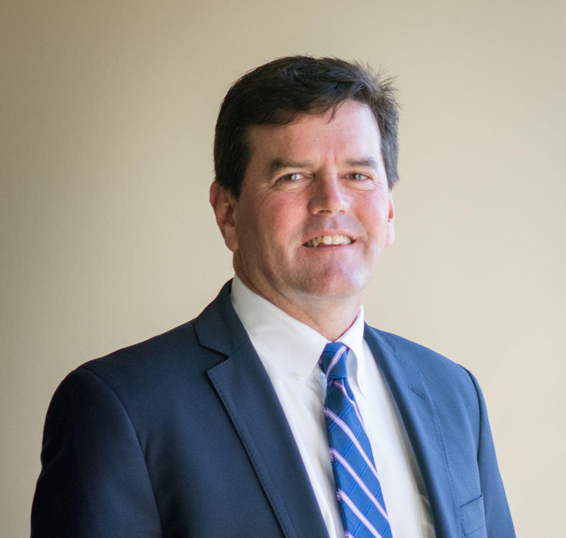 Man in a suit and tie smiling against a plain background.